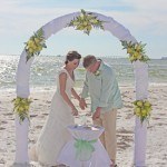 A couple cutting their wedding cake on the beach.