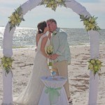 A couple kissing under an arch on the beach.