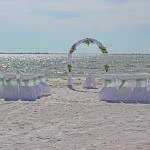 A beach wedding with white chairs and green bows
