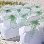 A group of white chairs with green bows on the beach.