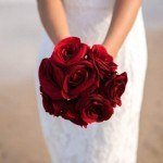 A bride holding her bouquet of red roses.