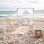 A beach wedding with white chairs and a canopy.