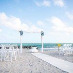 A beach wedding with white chairs and blue flowers.