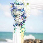 A white and blue flower arrangement on top of a wedding arch.