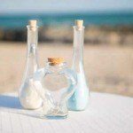 Three glass bottles on a table near the beach.