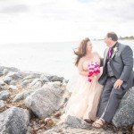 A bride and groom sitting on the rocks by the water.