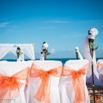 A wedding ceremony with orange bows on the chairs.