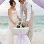 A couple cutting their wedding cake on the beach.
