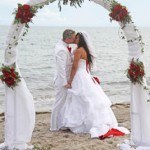 A couple kissing under an arch on the beach.