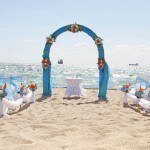 A wedding arch on the beach with chairs around it.