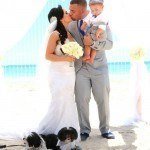A bride and groom kissing on the beach with their dogs.