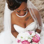 A bride sitting on the beach with her bouquet.