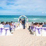 A wedding ceremony on the beach with purple and white decorations.