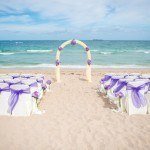 A beach wedding with purple and white chairs