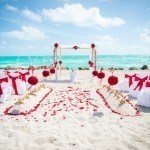 A beach wedding with red roses and white chairs