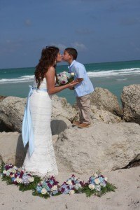 A young boy kissing the forehead of his mother on the beach.