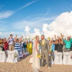 A bride and groom standing on the beach with their wedding party.