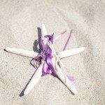 A purple ribbon tied to five white candles.
