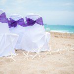 Two white chairs with purple bows on the beach