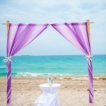 A purple and white wedding arch on the beach