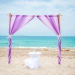 A purple and white wedding arch on the beach
