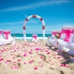 A beach wedding with pink flowers and white chairs