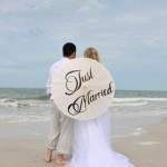 A couple is standing on the beach with just married umbrella.