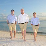 Three men in white shirts and khaki shorts on the beach.