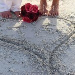 A couple is standing on the beach with their feet in sand.