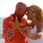 A man and woman holding starfish in front of the ocean.