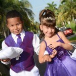 A boy and girl in purple dresses holding pillows.
