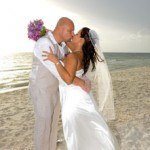 A bride and groom kissing on the beach.