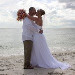 A newly married couple kissing on the beach.