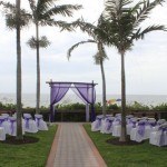 A wedding ceremony with purple drapes and white chairs.