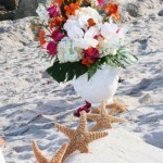 A vase of flowers on the beach with starfish