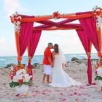 A couple is kissing under an orange and pink canopy.