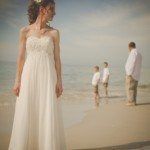 A bride and groom stand on the beach
