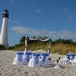 A beach wedding with white chairs and blue sashes
