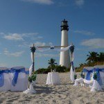 A wedding set up on the beach with a lighthouse in the background.