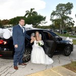 A bride and groom pose for the camera in front of their limo.